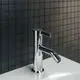 Bidetarmatur aus Chrom von Ideal Standard mit einem gebogenen Auslauf und einem Hebel zum Einstellen des Wasserflusses, montiert auf einem weißen Waschbecken und dunkler Wand.